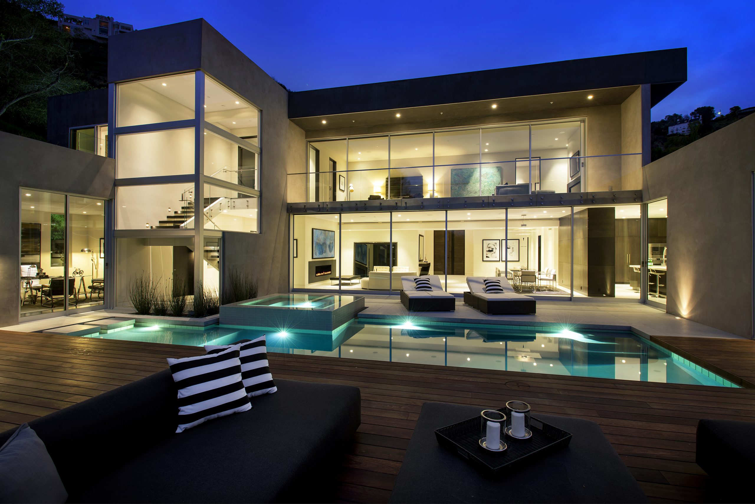 Modern architectural home at twilight with glass walls, illuminated pool and luxurious outdoor space
